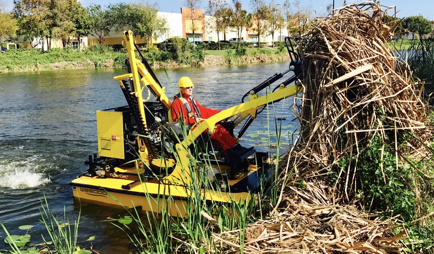 Yellow WeeDoo TigerCat workboat lifting a large bundle of shoreline vegetation from the water